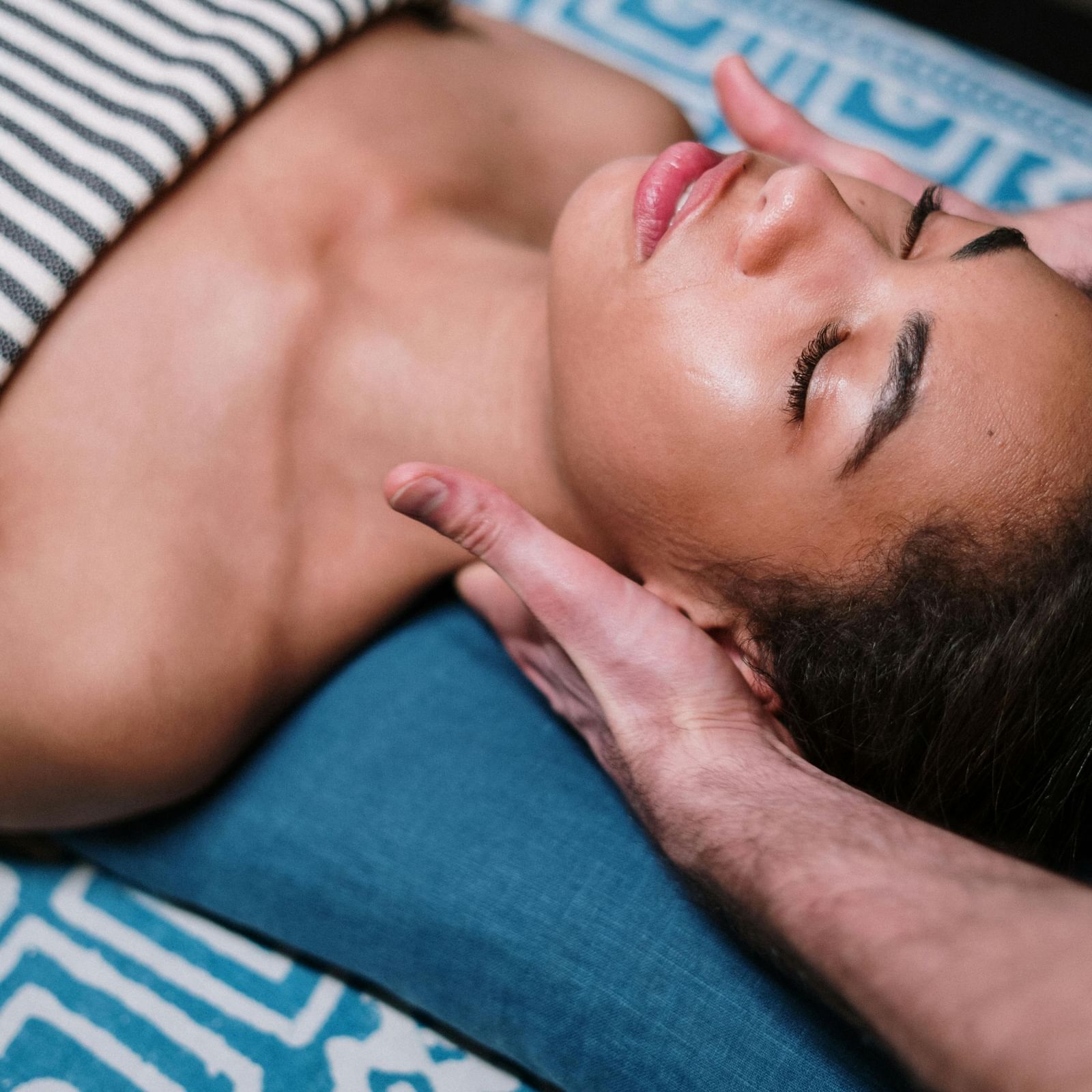 Woman receiving a head massage on a blue pillow at a spa.