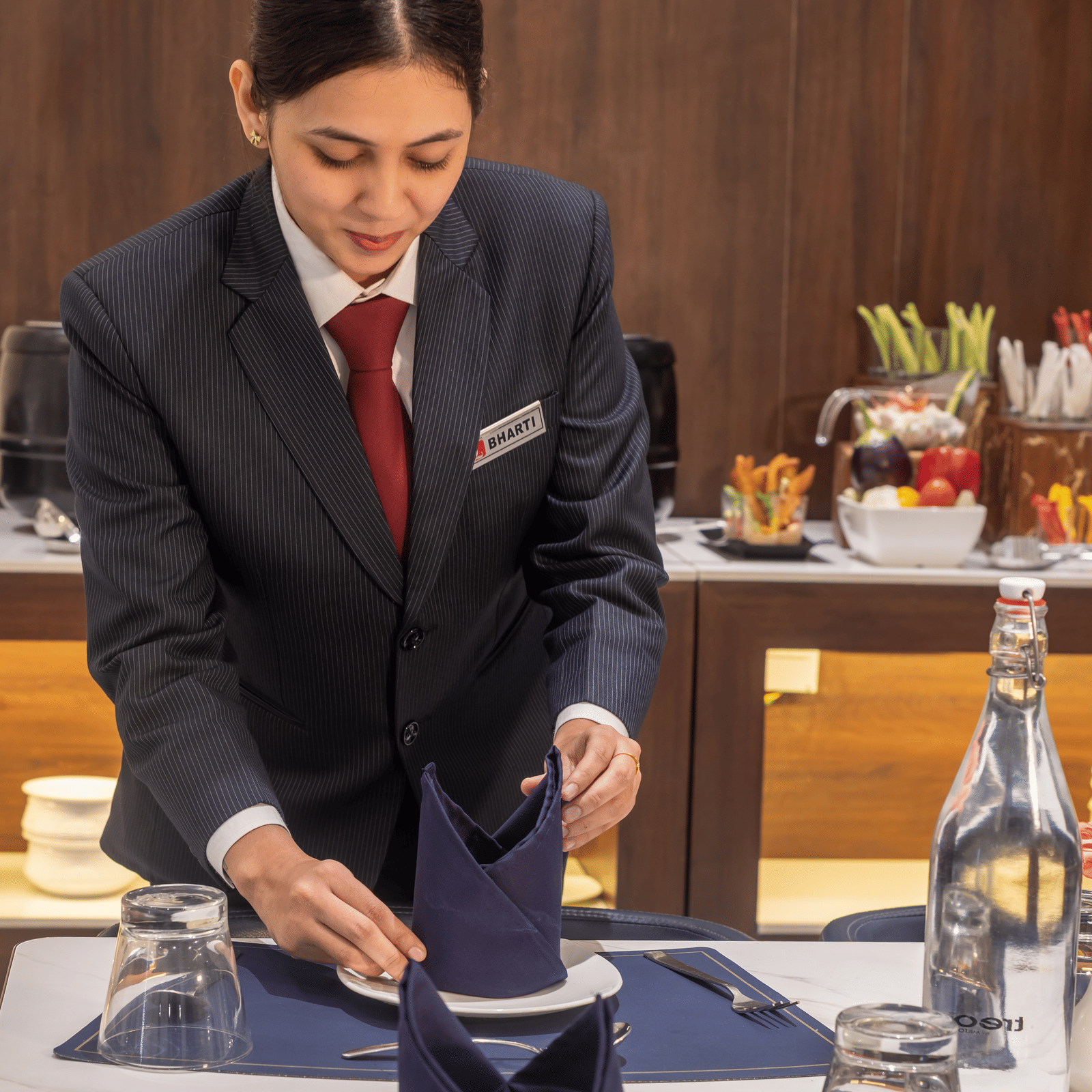 A hotel staff member in formal attire carefully setting up a dining table at Lords Studio Inn, Jamnagar.