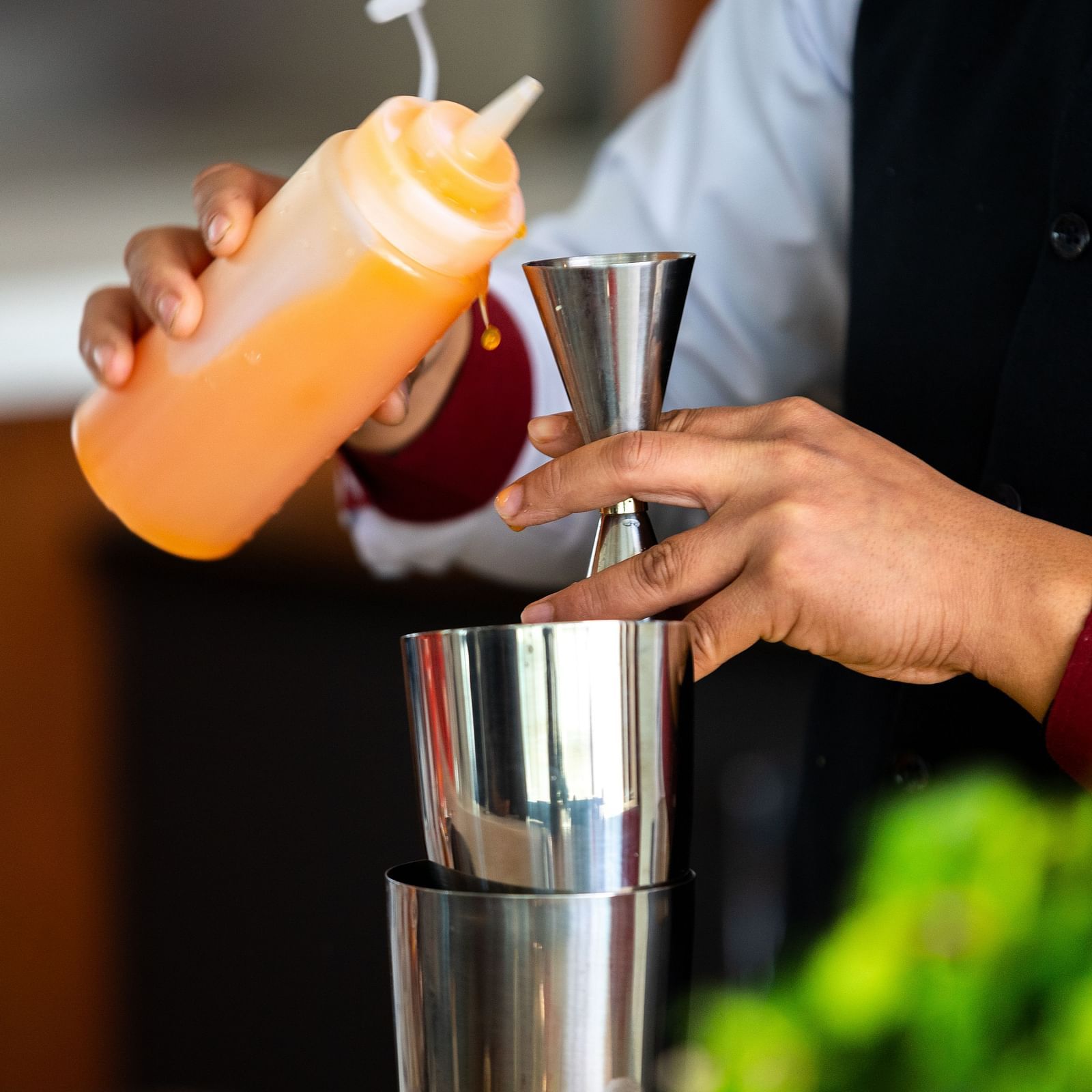 A bartender pours an orange liquid from a squeeze bottle into a jigger over a metal shaker at Mandala Norling Lords Prime in Kathmandu.