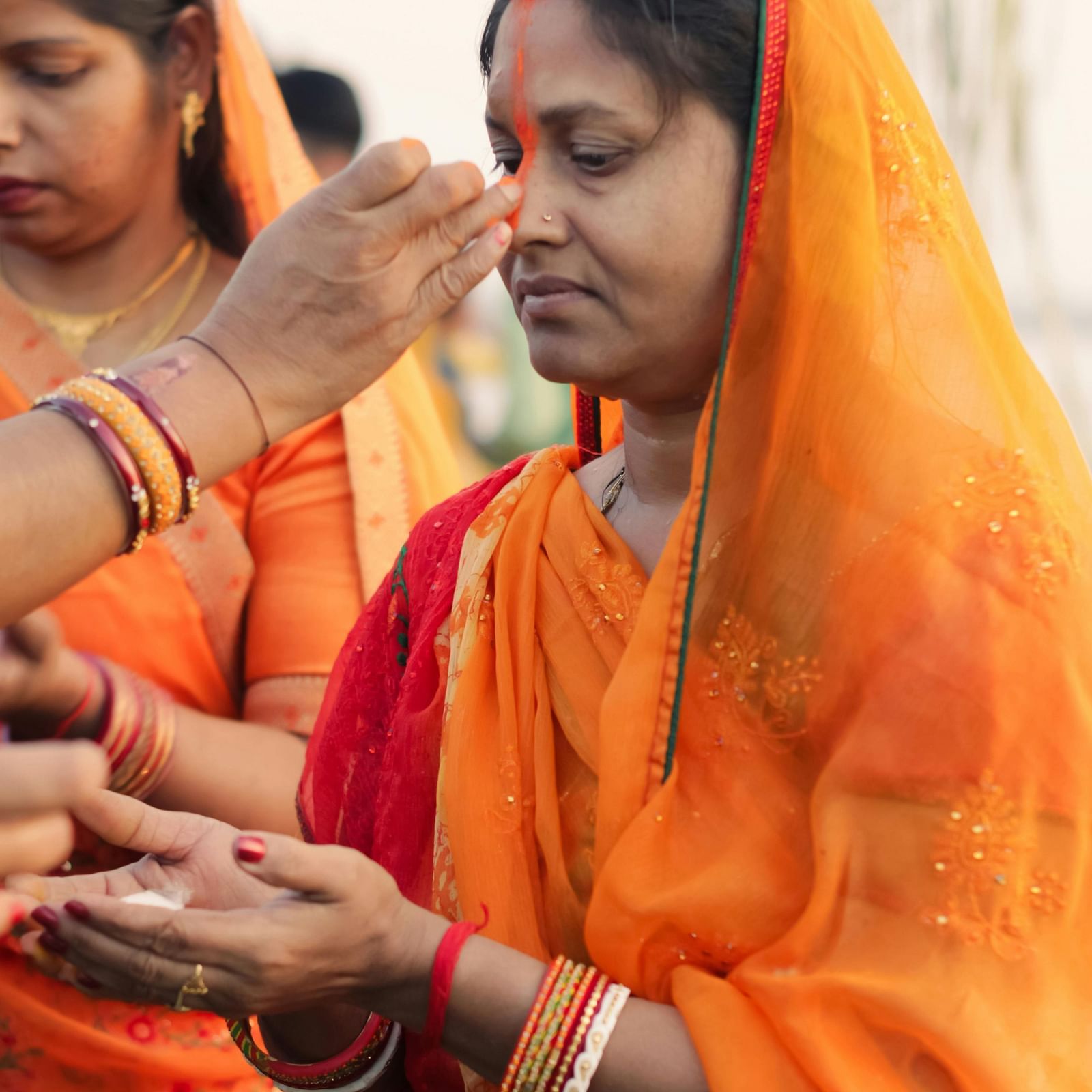 Women dressed in vibrant orange sarees participating in a religious ceremony