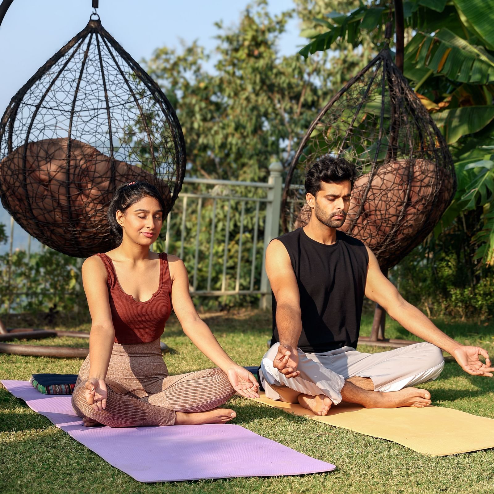 two people sitting on a yoga mat in the lawns and meditating