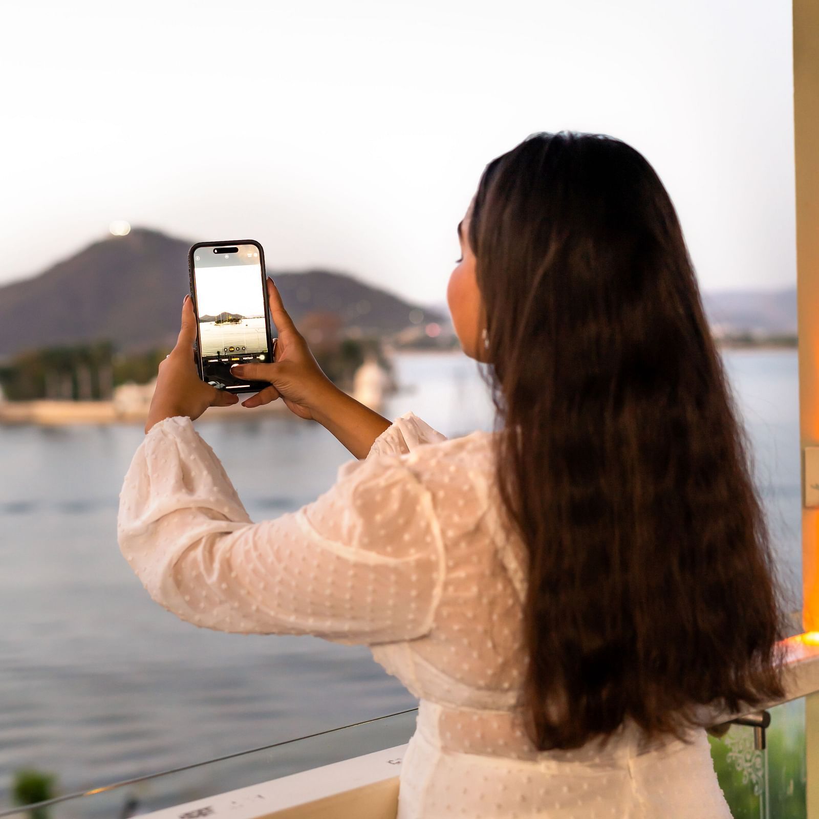 Guest taking a photo of the stunning lakeside view from the terrace of Panna Vilas Palace during golden hour.