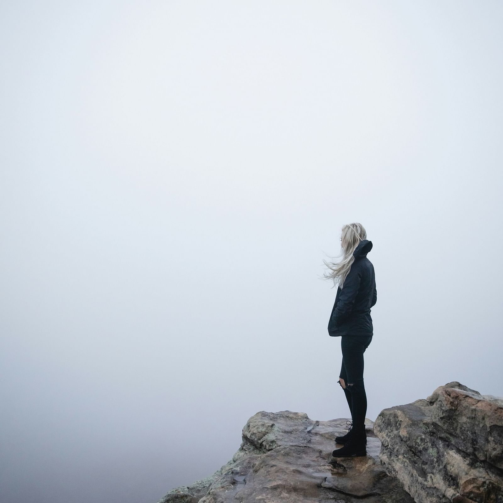 A person standing at the edge of a fog-covered hill, surrounded by mist.