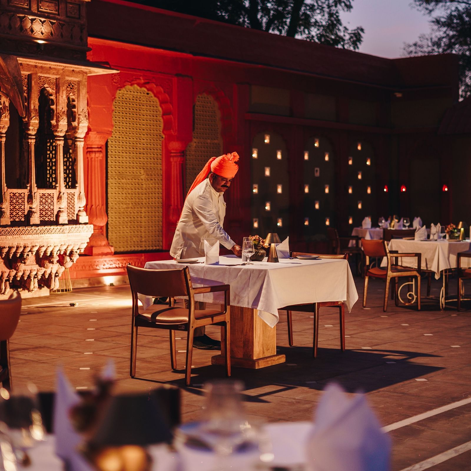 An outdoor dining setup with a traditionally dressed server at Surpura Bagh.