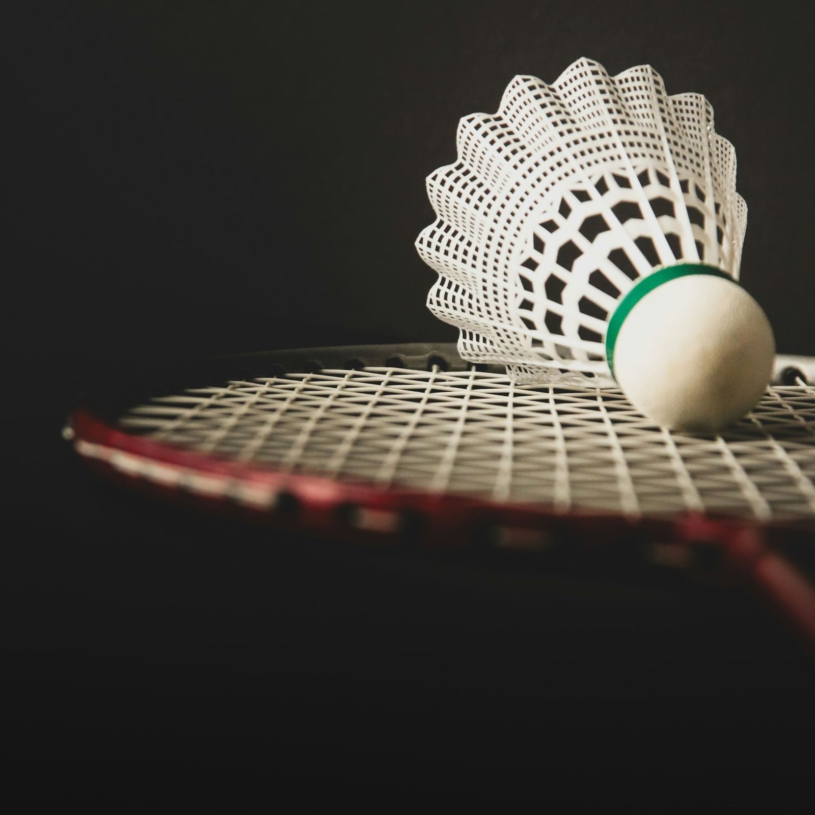 A shuttlecock placed on a racket against a dark background.