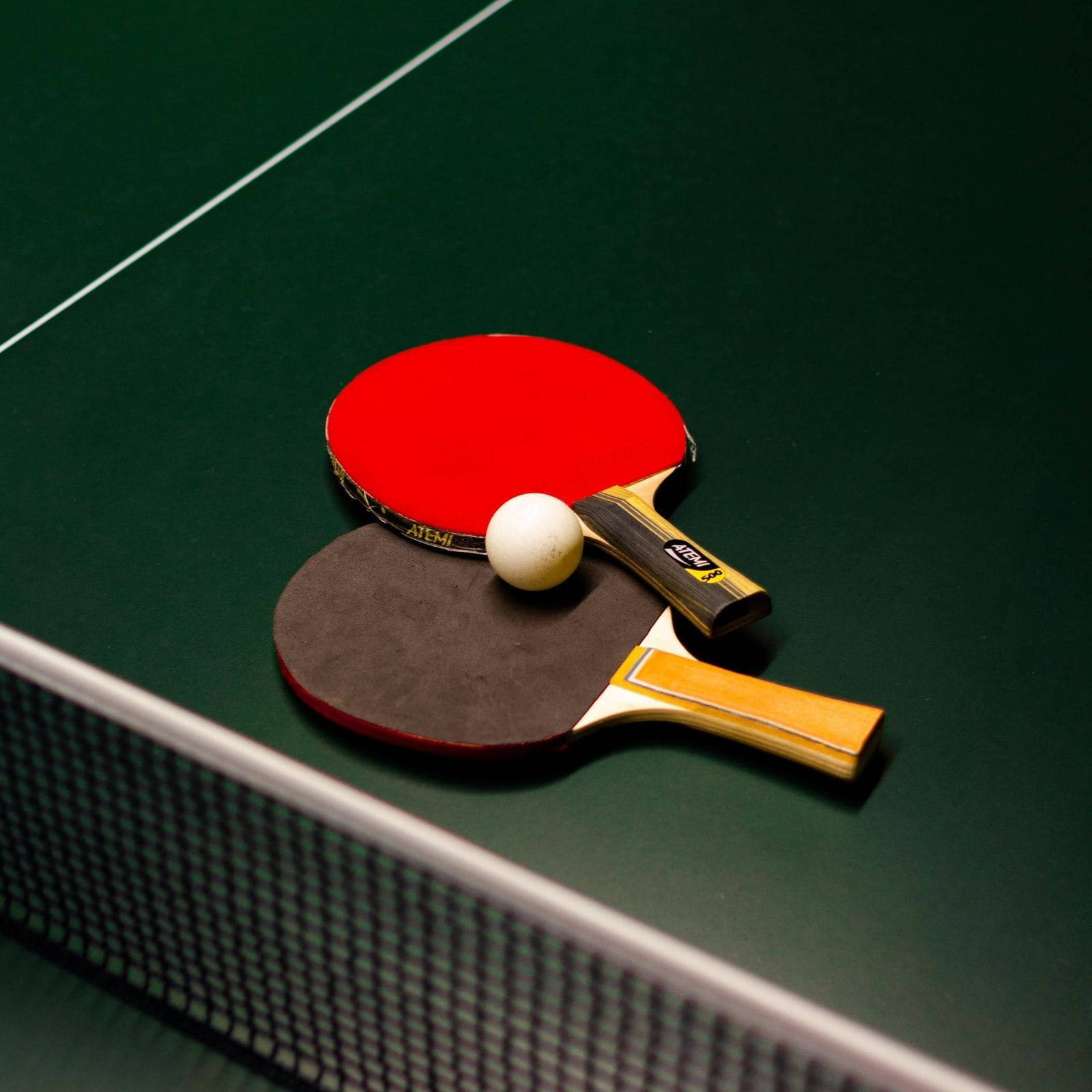 Table tennis ball and bats placed on a T.T table featuring its net.