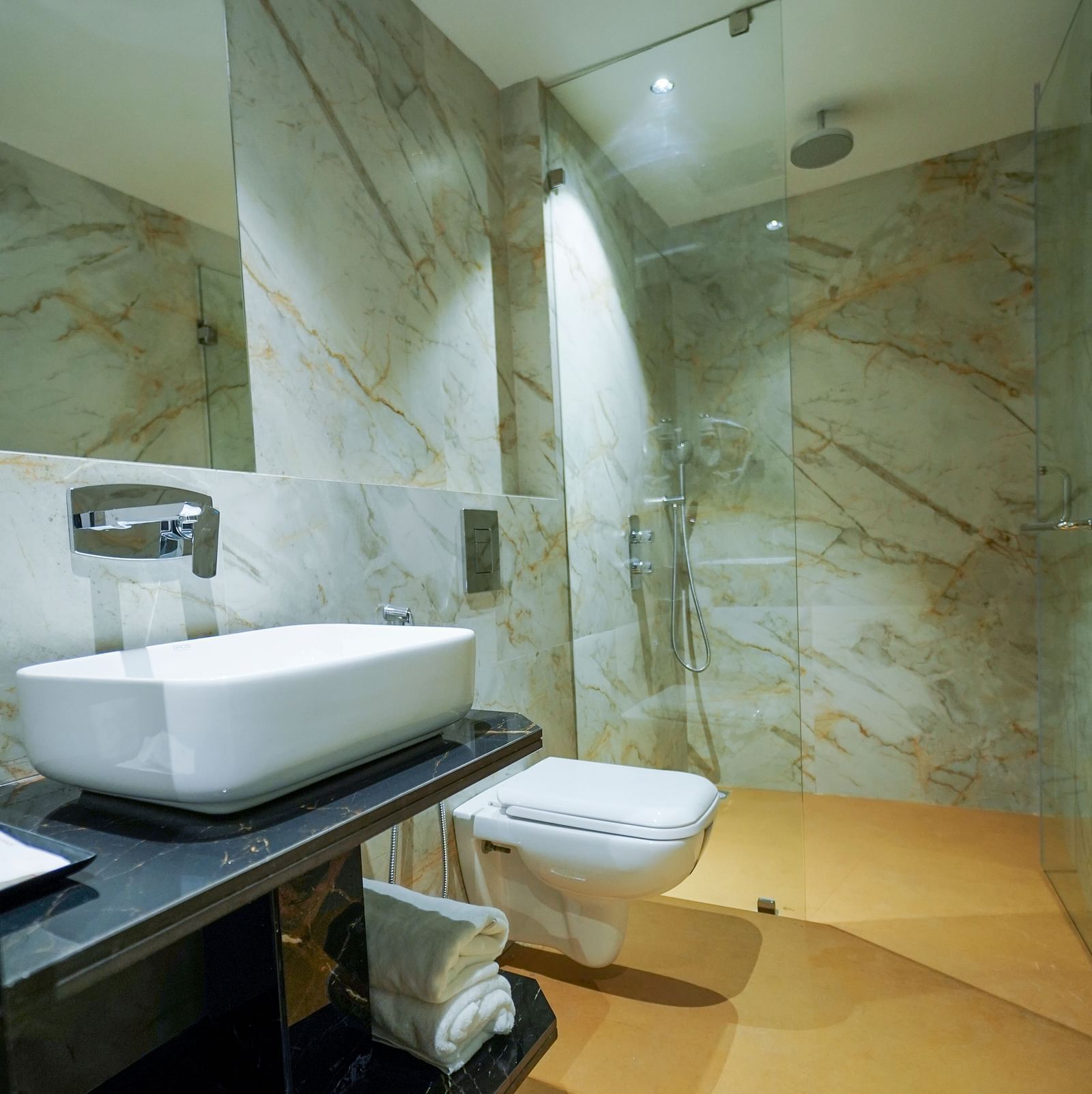 A bathroom has a rectangular sink with a modern faucet, a mirror, a toilet, and a shower area with a glass partition - Hotel Park Inn, Nellore.