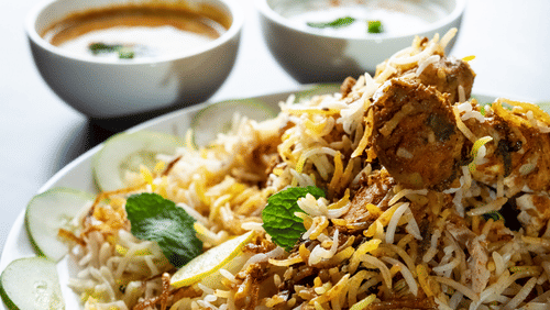 A plate of noodles with vegetables served with two small bowls of sauces on the side.