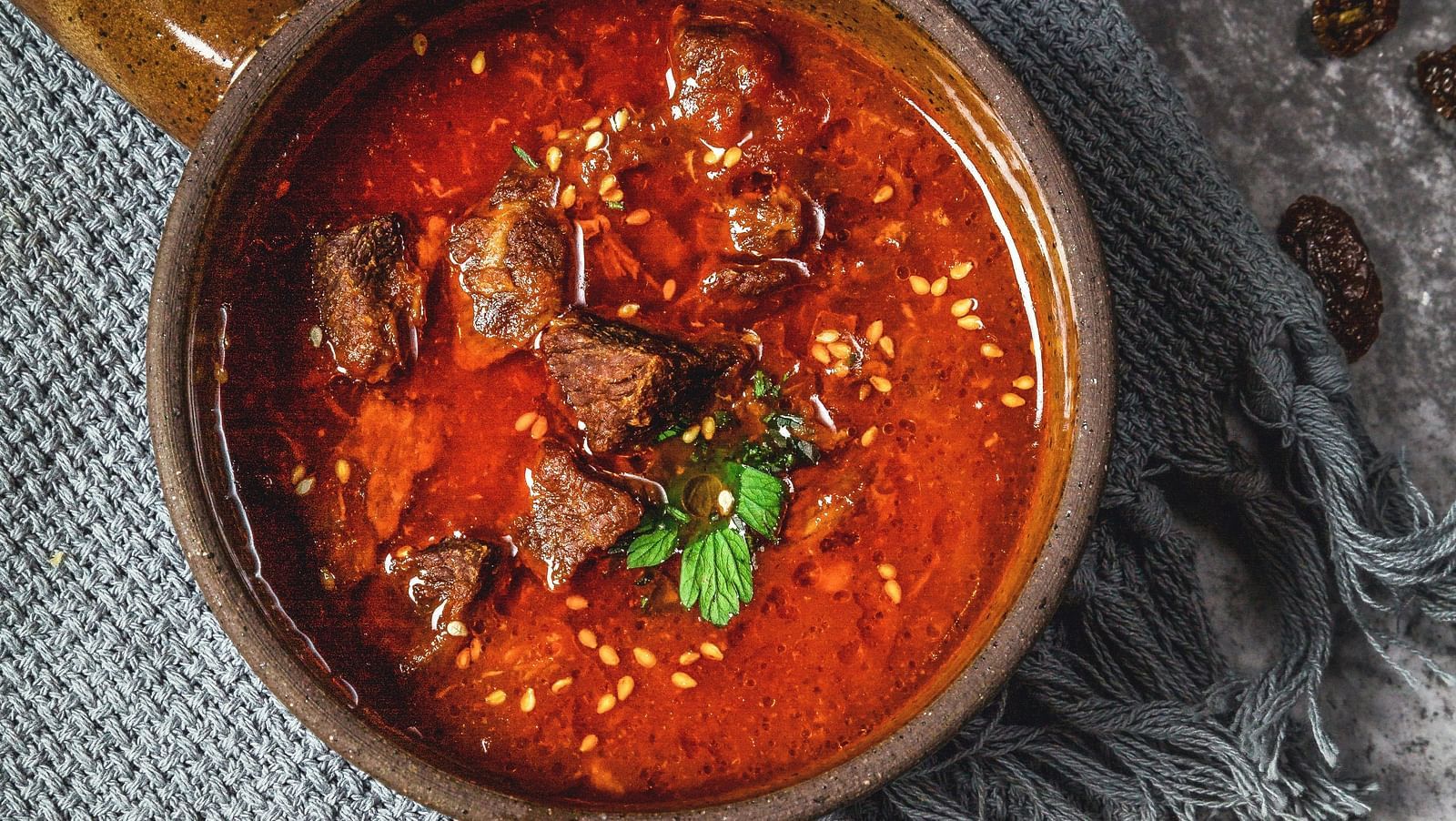 Top view of mutton curry kept in a bowl on the table with a knife and fork next to it