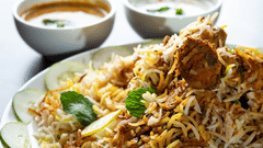 A plate of noodles with vegetables served with two small bowls of sauces on the side.