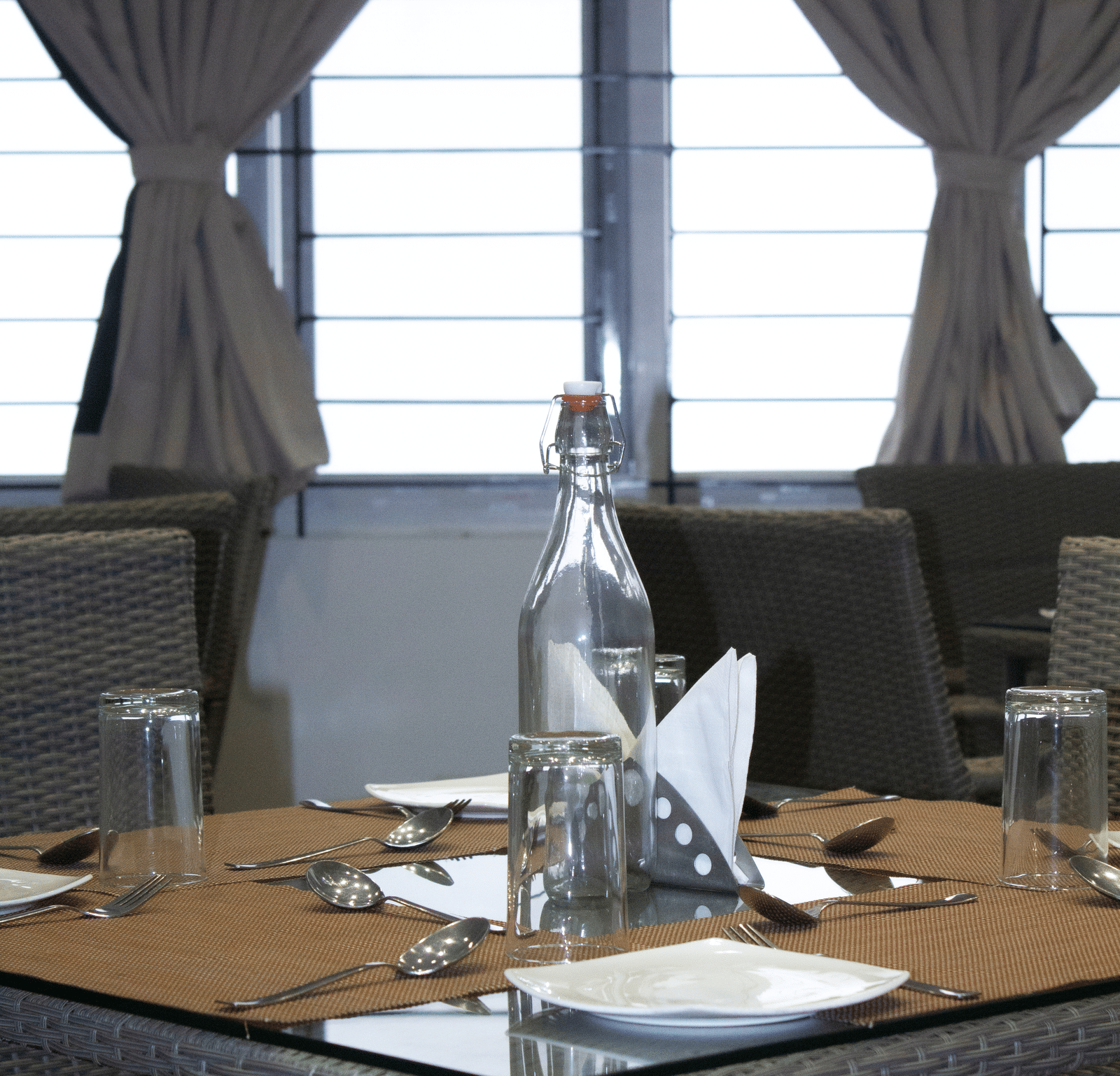 Close up of a dining table at the Spice and Slice Restaurant featuring cutlery and a glass water bottle in the middle of the table at WOW Naturefull Resorts, Yercaud.