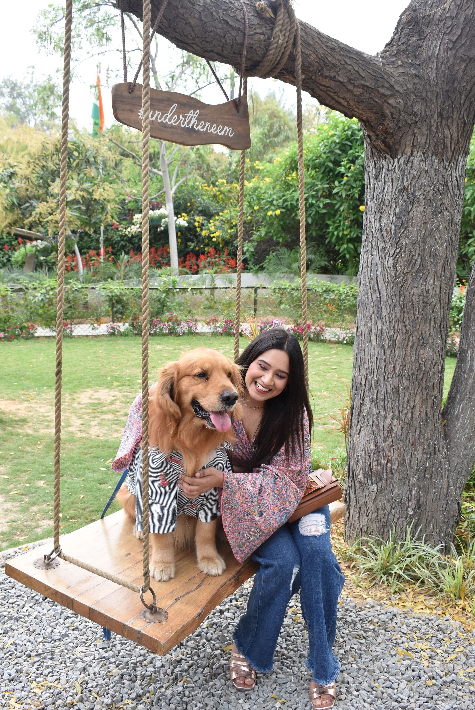 Portrait view of a female and a dog sitting on the large outdoor swing hung on a tree with a lawn area in the backdrop at Karma Chalets.