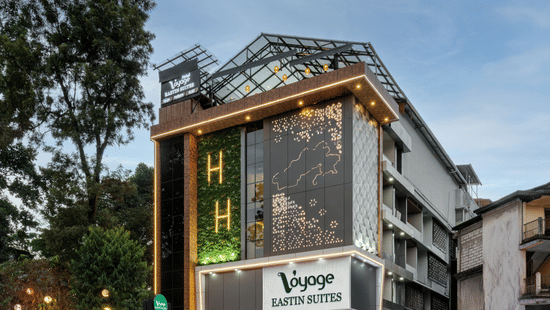 The exterior of a multi-storey hotel building with large windows and an entrance on the ground floor, surrounded by trees and greenery | Voyage Eastin Suites