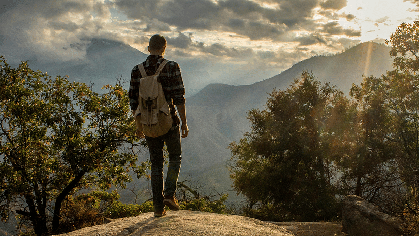 View of a person standing on a cliff watching the sun and the clouds.