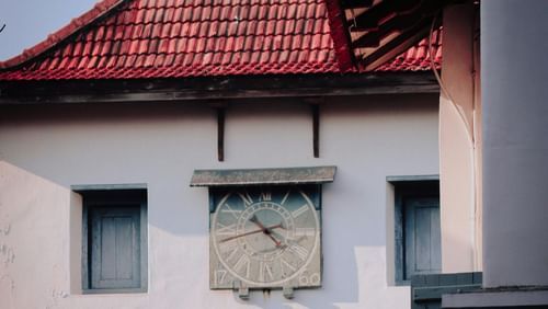 A vintage clock hanging on the wall outside a traditionally built Kerala building.