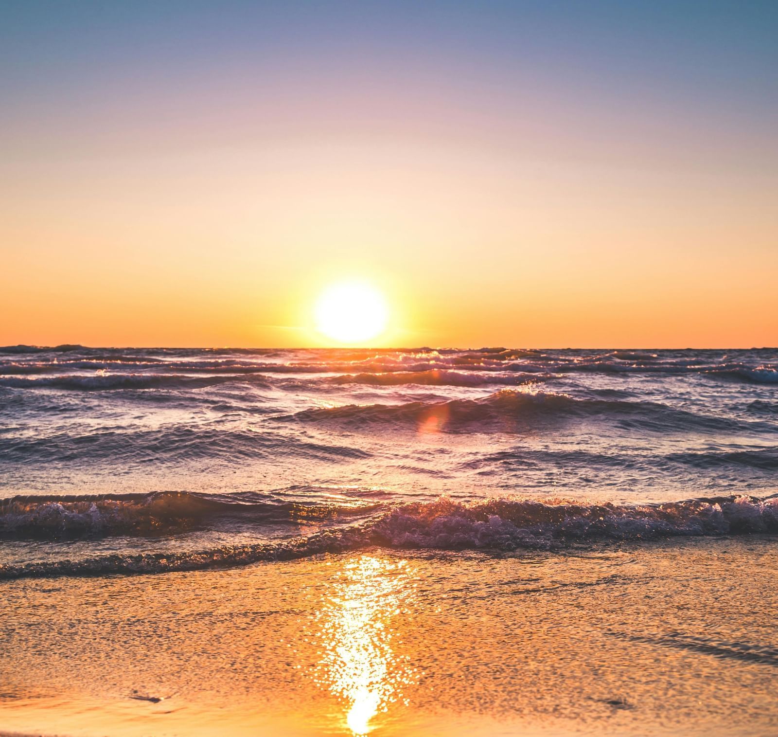 A mesmerising sunset on a beach with the golden sun rays reflecting off the surface of the ocean.