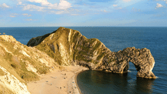 A natural formation of rocks near a beach with white clouds on blue sky in the background