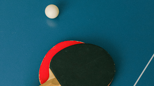 A high-angle shot depicts 2 table tennis bats, a small circular ball, and a table tennis table with a clean dividing line.