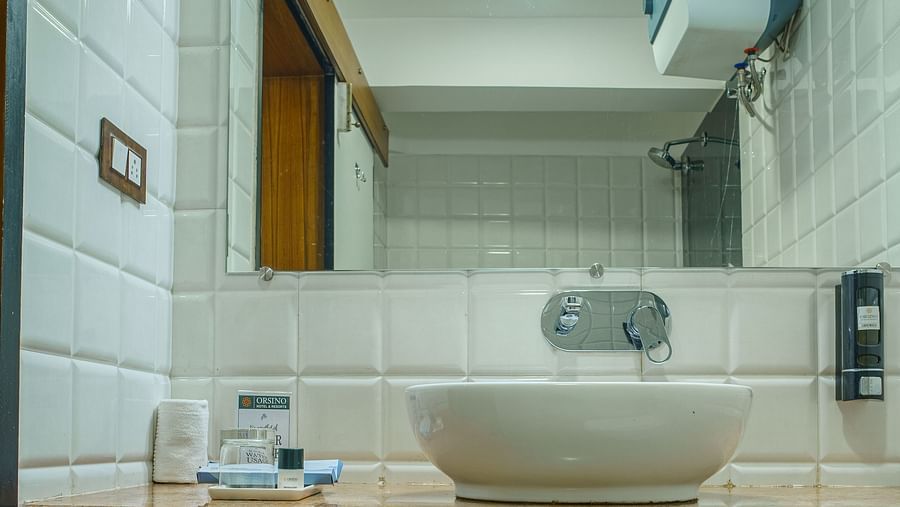 A bathroom at Orsino Spa Resort with a white sink, a mirror, and a shelf beneath the sink.