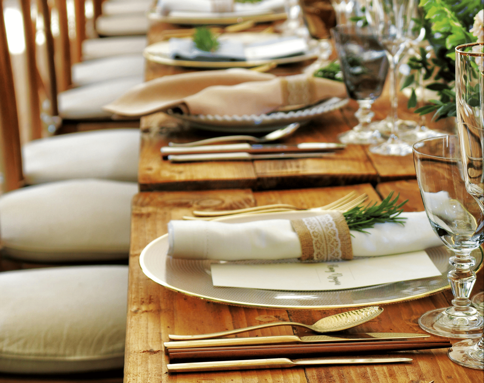 A long wooden table with beautifully set cutlery with small fern leaves in vases.