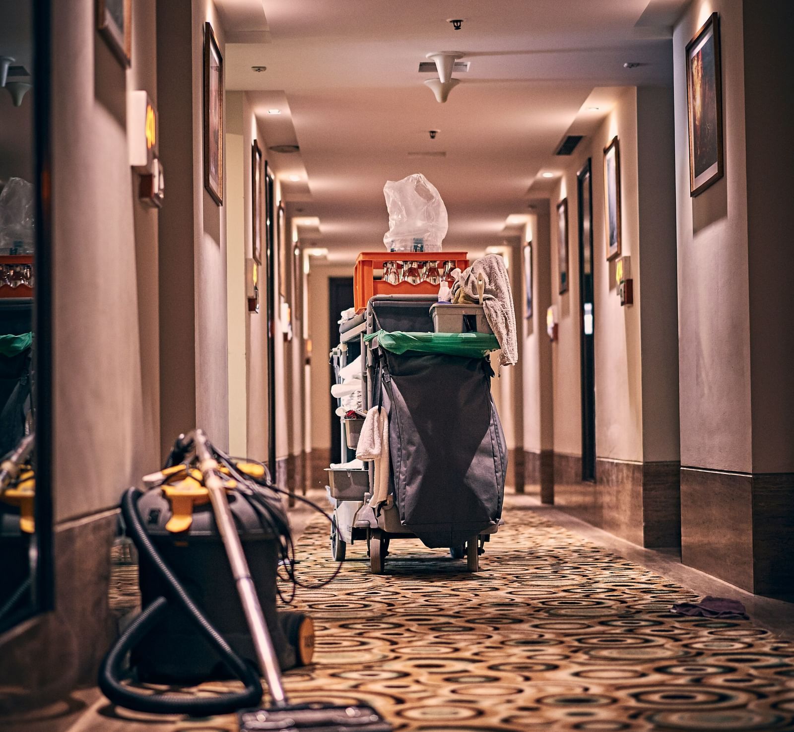 A housekeeping trolley kept in the middle of the hotel corridor along with a vacuum cleaner kept on the floor.