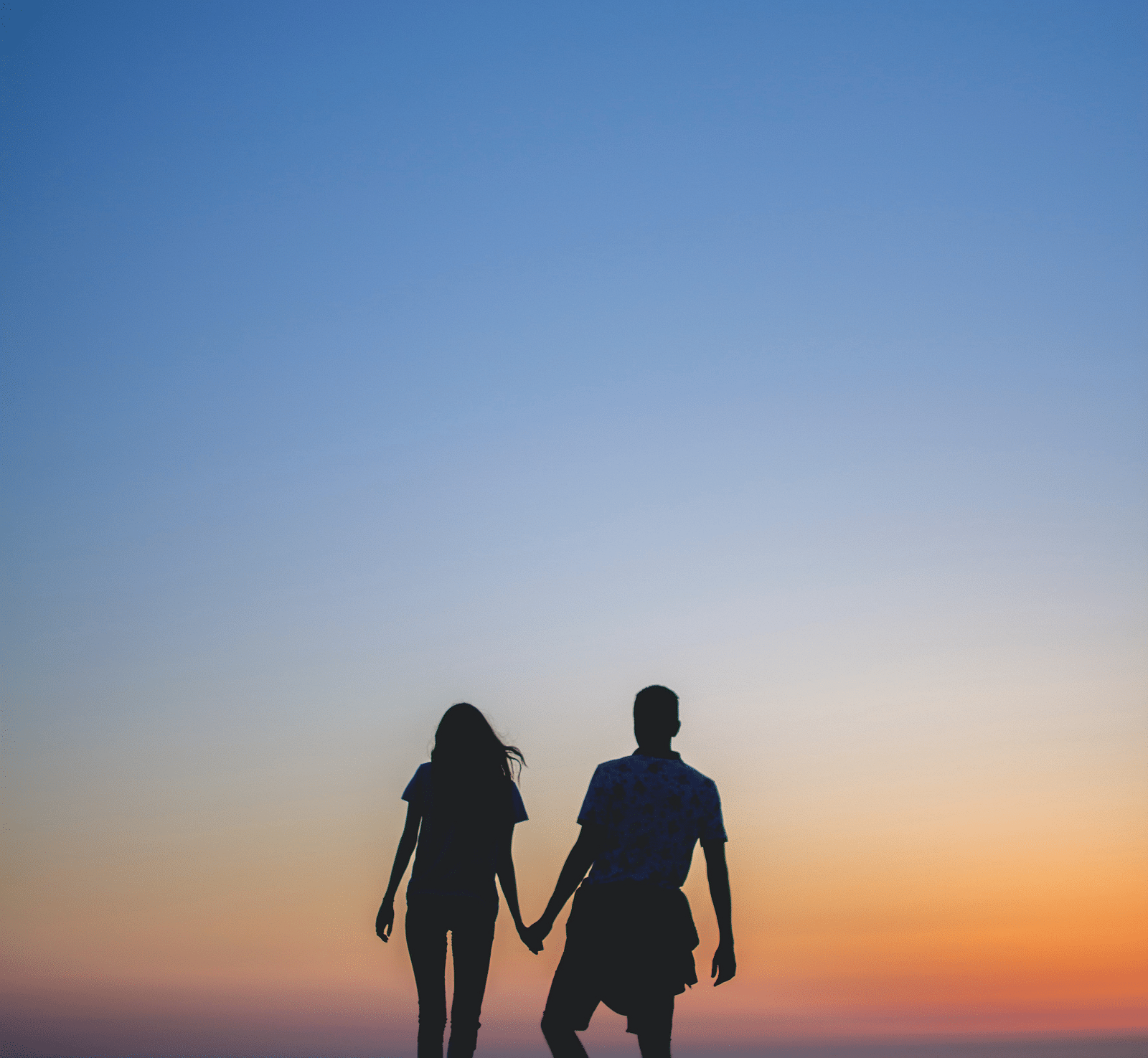 silhouette of a couple holding hands as they walk in front of a beautiful sunset in the background