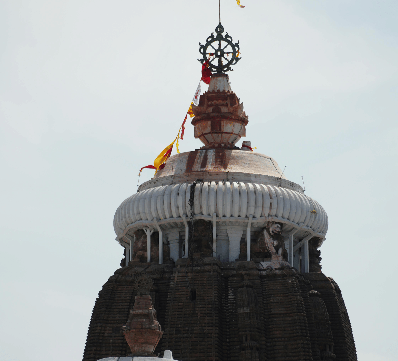 The white upper portion of a traditional Indian temple featuring intricate carvings, against a bright sky.