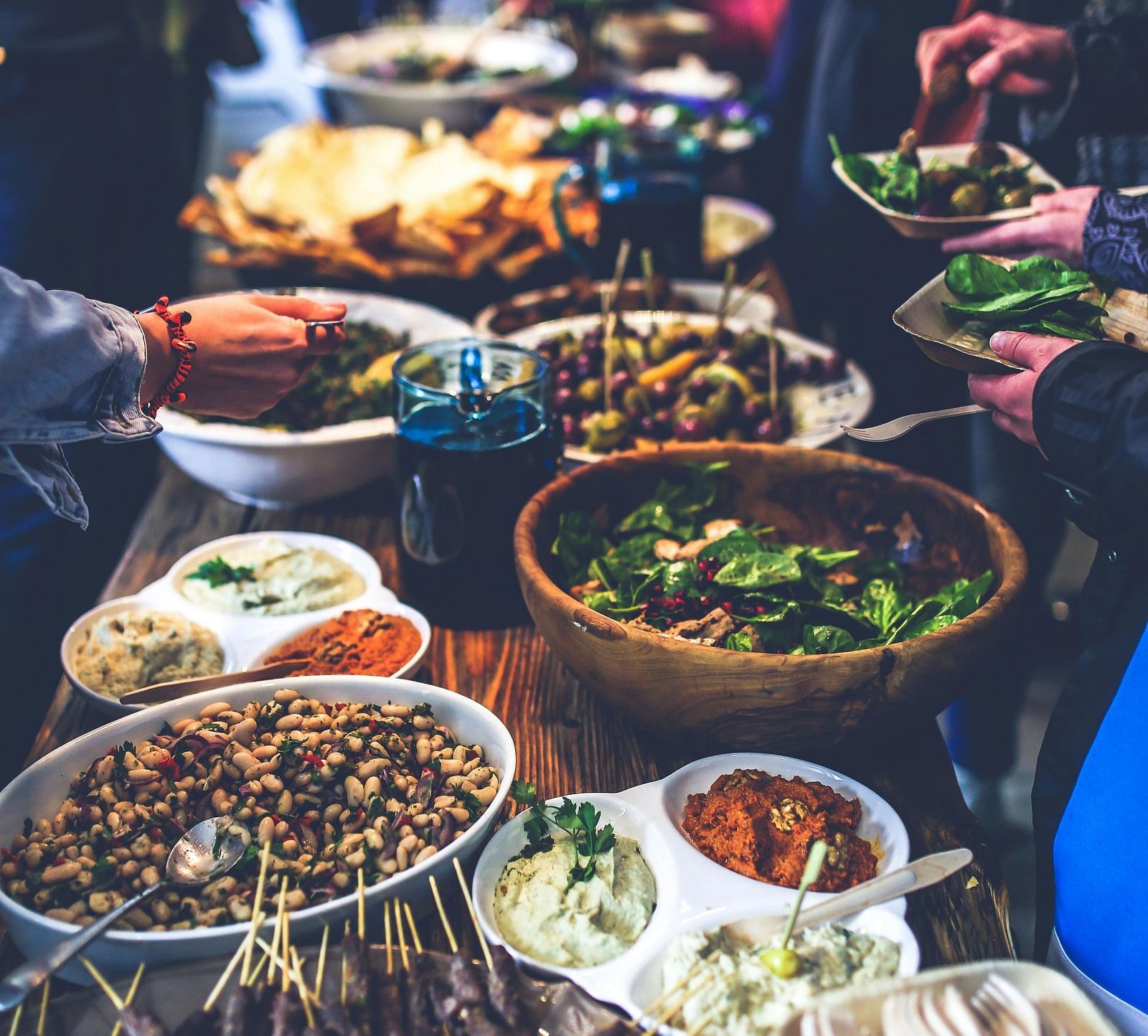 An image of a buffet table where several dishes are placed and people around are helping themselves