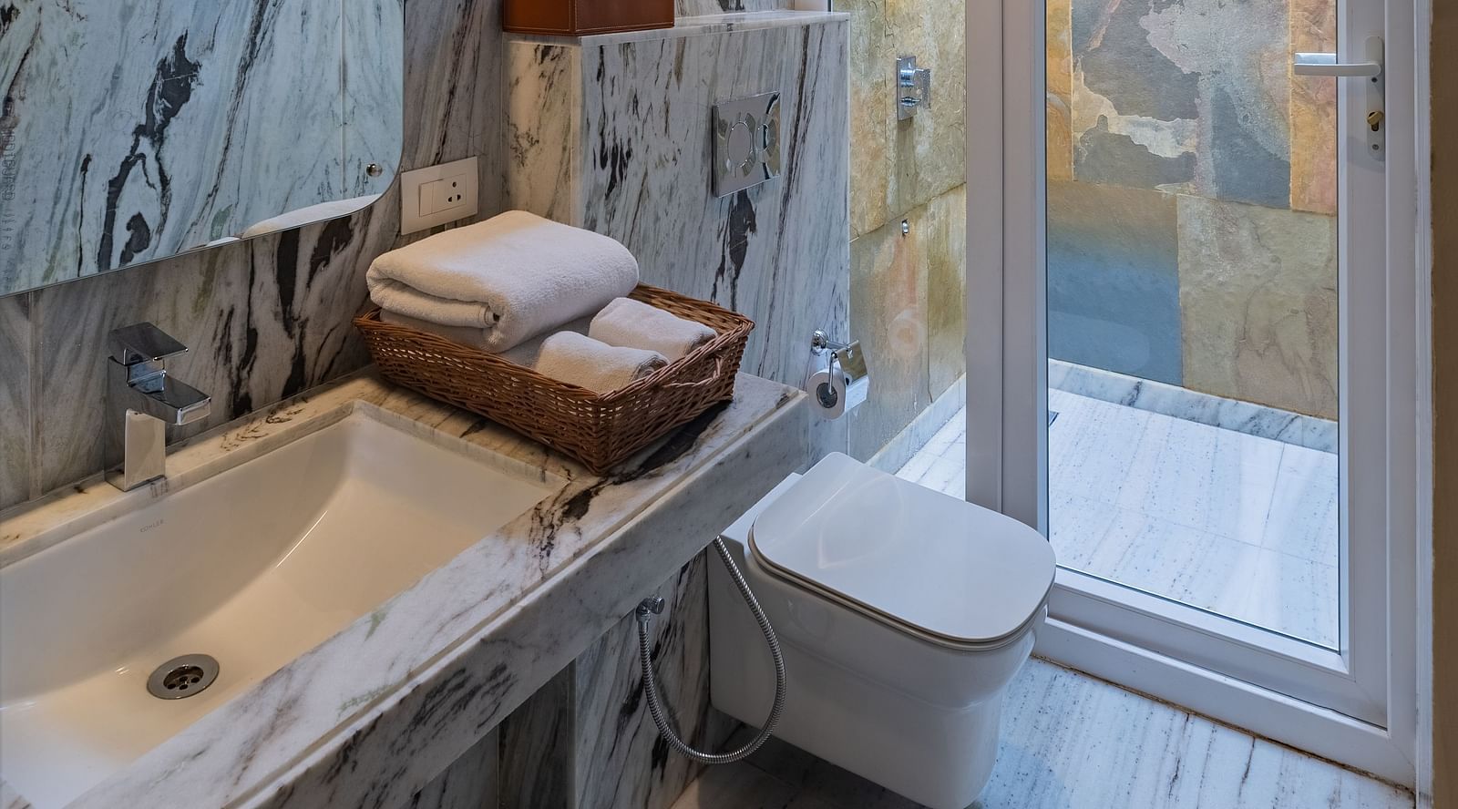 image of the well appointed modern bathroom featuring a wash basin and a commode besides a full length window at the luxury suite villa at aranya vilas