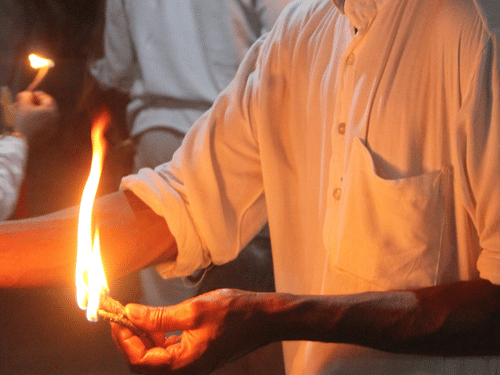 A man in a white shirt holding a small flickering flame during a religious ceremony with pink drapes in the background.