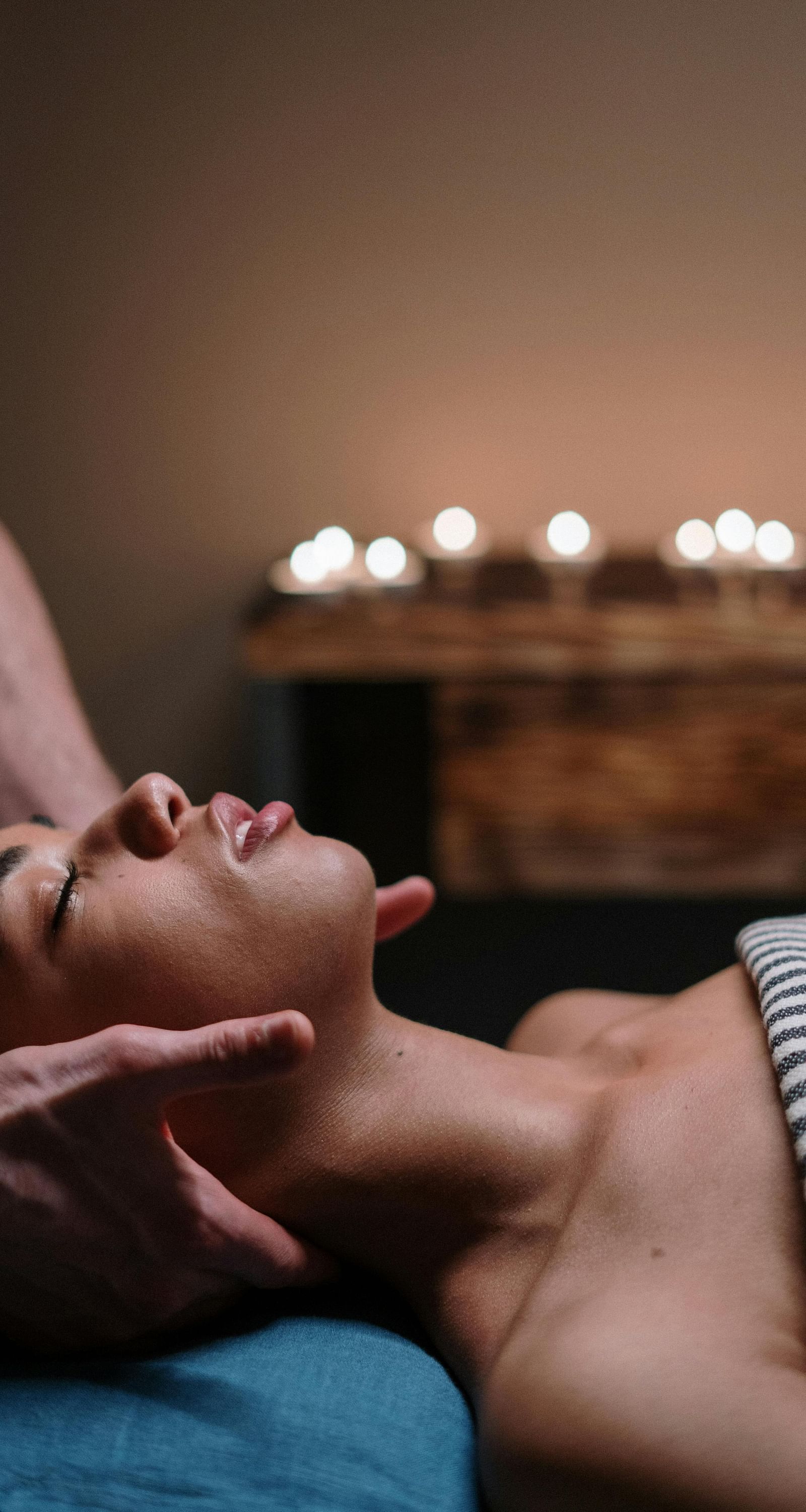 a woman with her eyes closed lying down on a bed as a masseuse massages her neck