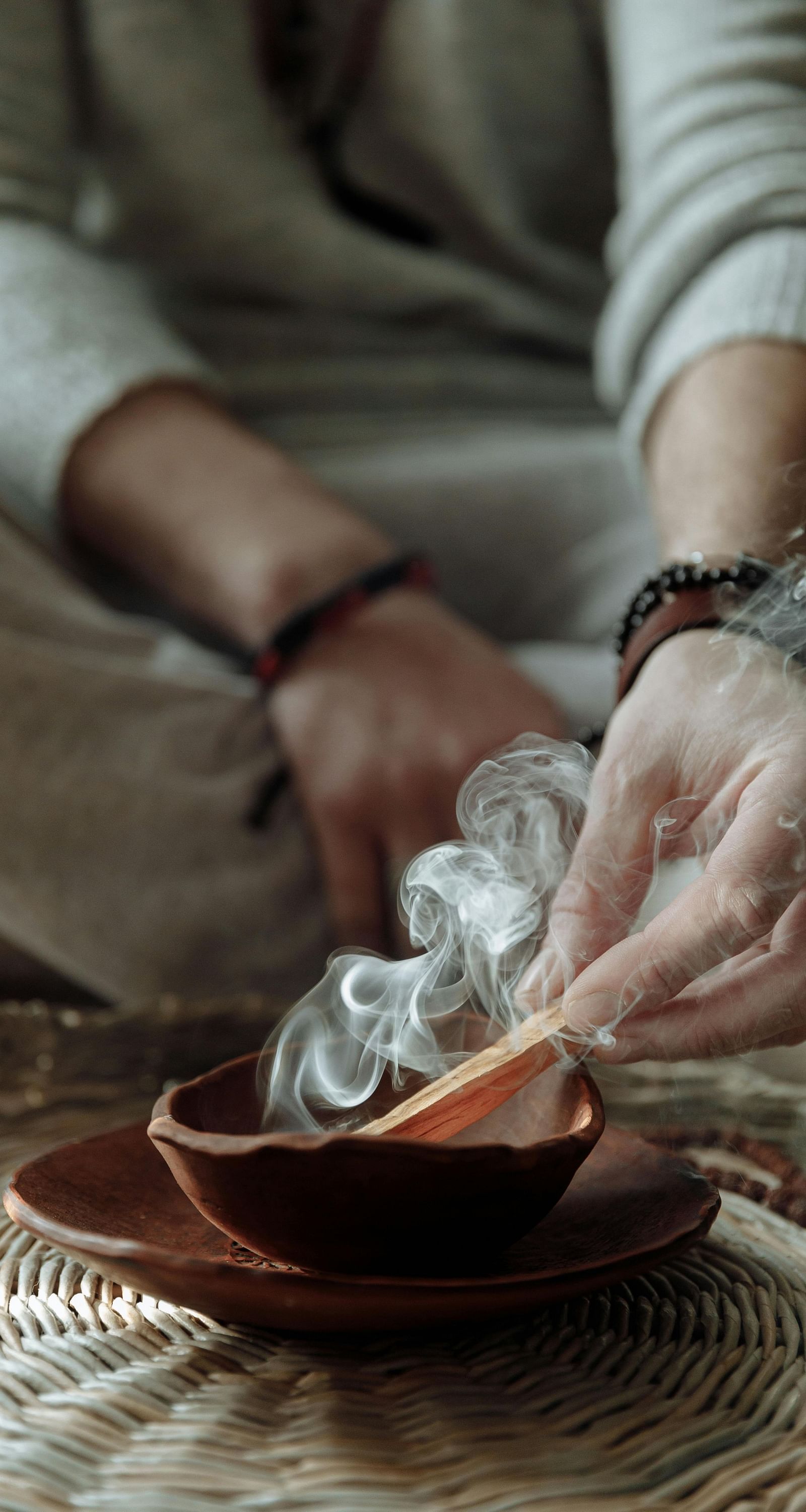 a person sitting on a huge mat burning incense sticks into a bowl