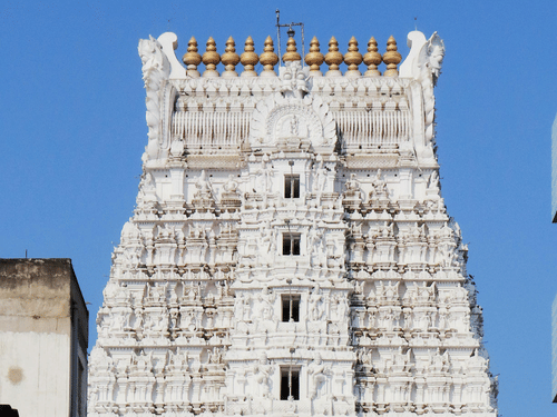 A view of the tall white gopuram South Indian temple with intricate carvings under the blue sky.