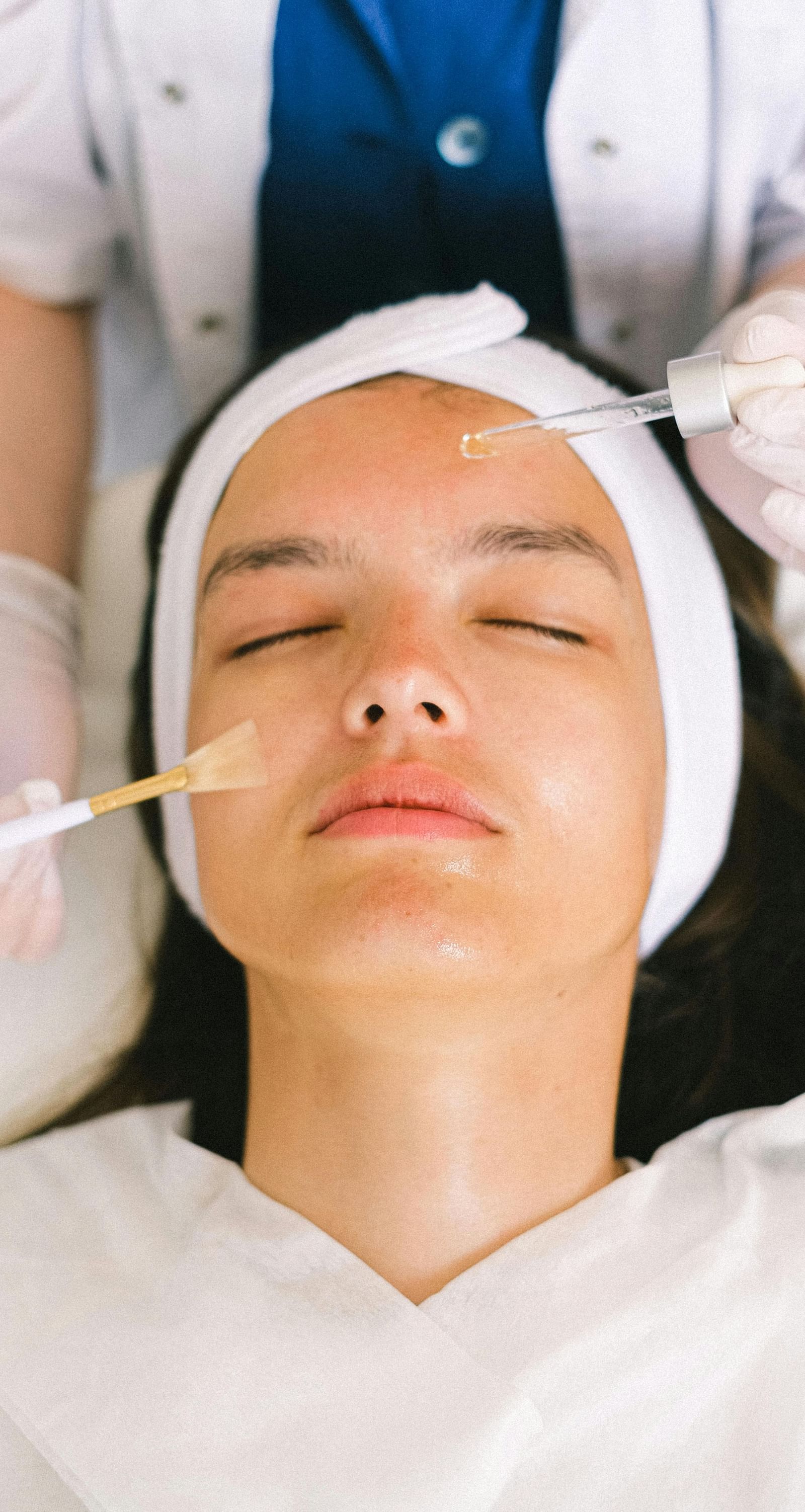 A woman getting a facial done where an expert is applying products with brushes