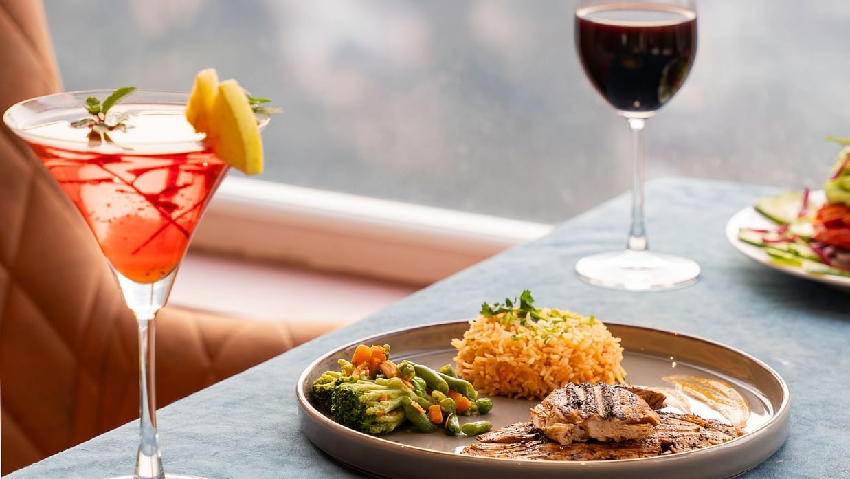 A close-up shows a plate of food and a glass of wine on a table.