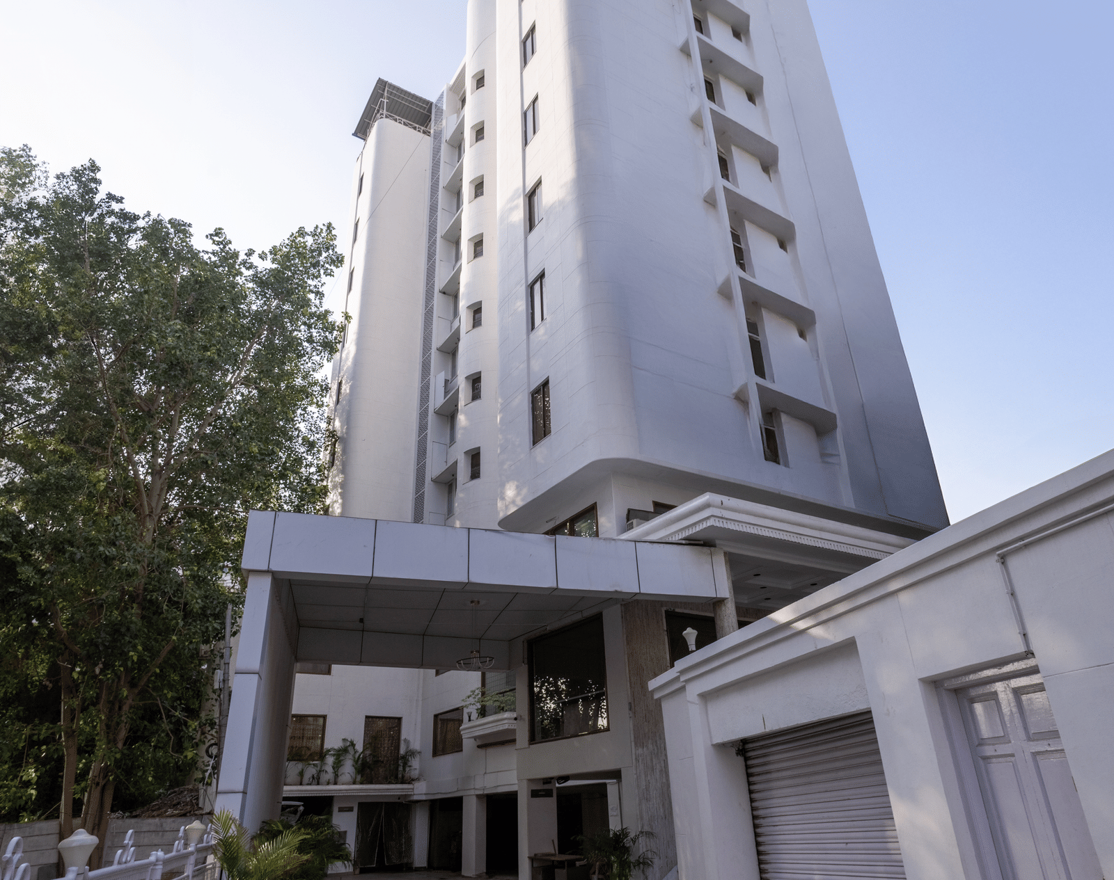 Exterior view of the tall, white hotel building standing against a clear sky, with a driveway leading to the entrance at Pravasa Stay, Vadodara.