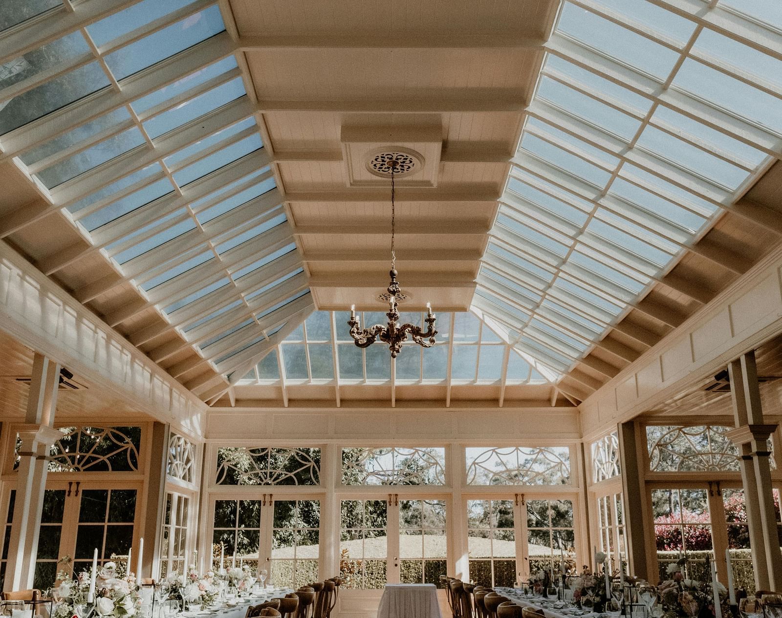 Interior view of a formal dining space with a glass roof and rows of set tables and chairs.
