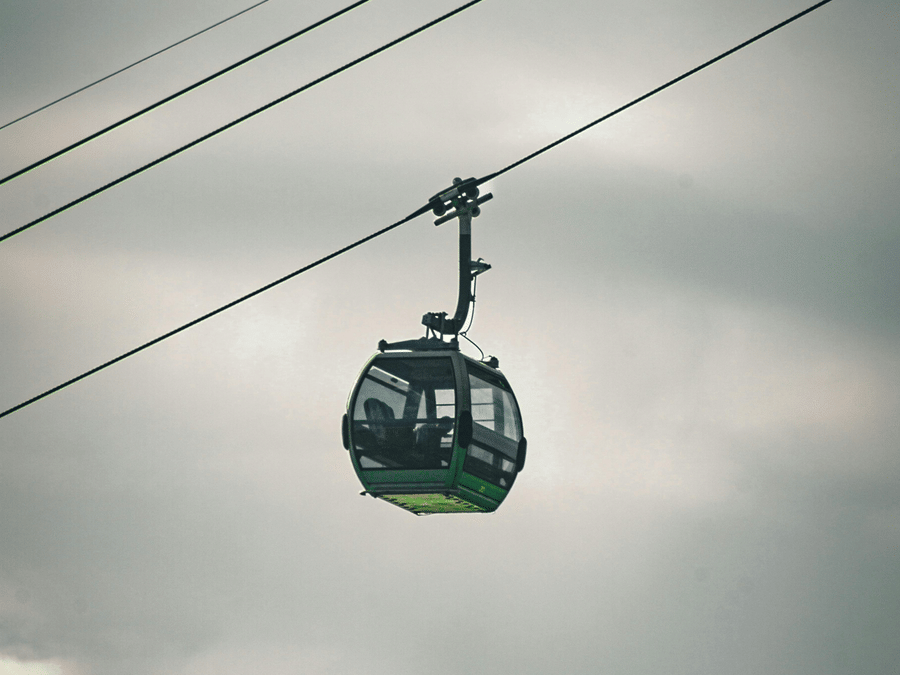 A cable car suspended in the air against a cloudy sky.