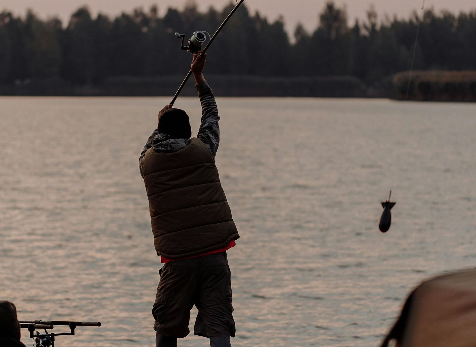 A man fishing at the lake at dusk.