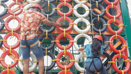 A group of people climbing a large vertical wall made of tires at Black Thunder Water Theme Park, showcasing an adventurous outdoor activity.