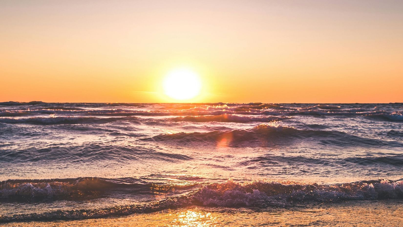 A beach with golden sand, gentle waves, and clear blue sky