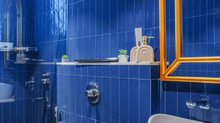 Bathroom at Unseen Boutique Hotel with bright blue tiled walls, modern sink, toilet, and yellow framed mirror.