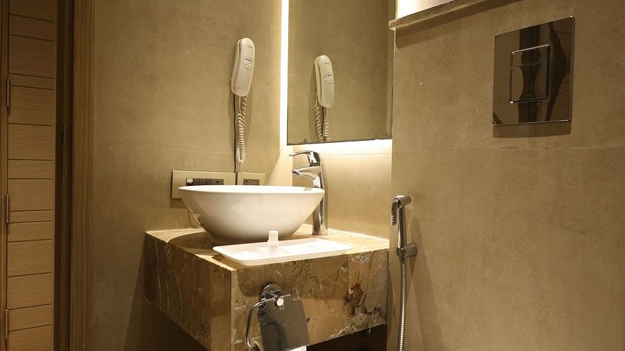 A modern hotel bathroom featuring a white vessel sink on a marble vanity, a toilet, and a mirror with backlighting. (Hotel Saket 27, New Delhi)