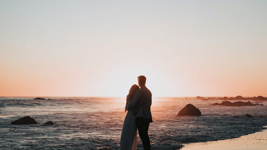 A couple embracing on the beach at sunset, creating a romantic and picturesque moment by the ocean.