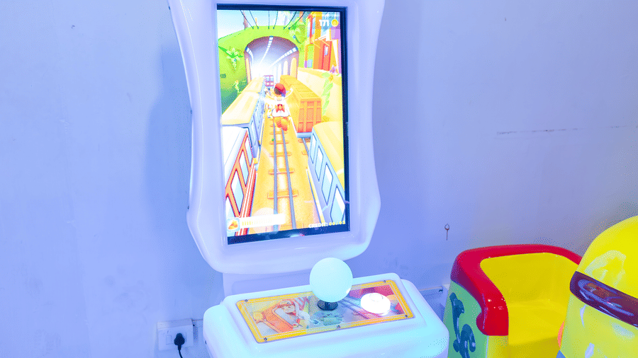 Parkour arcade game machine with a large screen and joystick, beside a yellow character-themed ride, in the arcade at DSF Grand Plaza, Tuticorin.