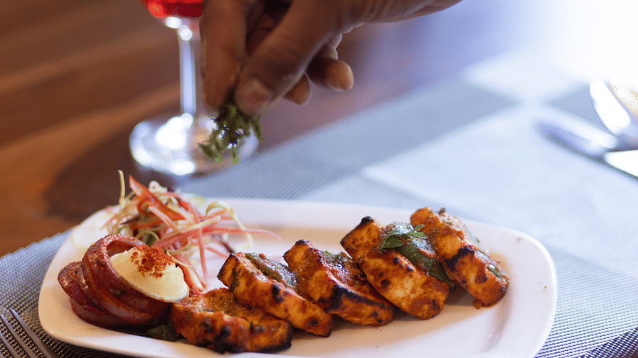 Hand of a person over a plate of grilled food served on a wooden dining table at Estherea Bagh, Ranthambore.