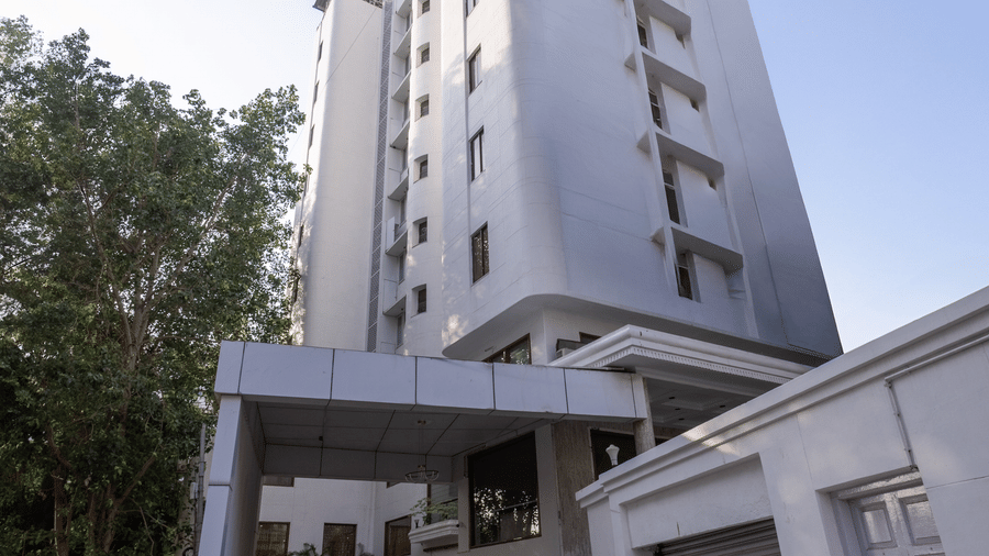 Exterior view of the tall, white hotel building standing against a clear sky, with a driveway leading to the entrance at Pravasa Stay, Vadodara.