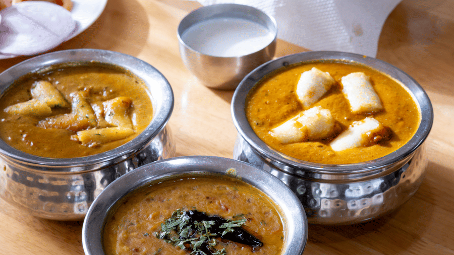 Traditional Indian food: metal bowls with curry and dal, with flatbread (roti) and fresh salad on a wooden surface at Pravasa Stay, Vadodara.