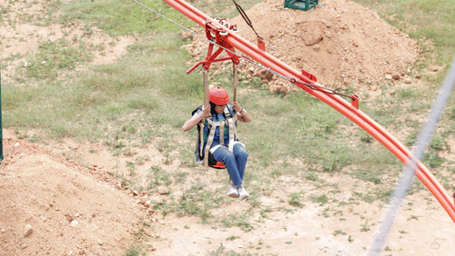A woman enjoying a seated zip line ride at Black Thunder Water Theme Park, soaring over the park with excitement.
