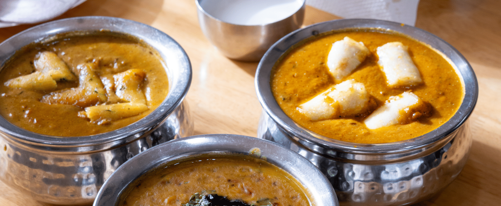 Traditional Indian food: metal bowls with curry and dal, with flatbread (roti) and fresh salad on a wooden surface at Pravasa Stay, Vadodara.